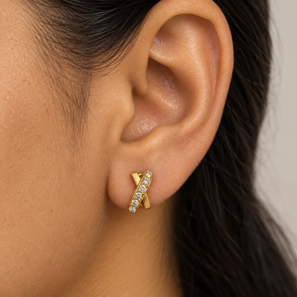 A close-up of a person's ear wearing a gold ear cuff earring adorned with small clear stones.