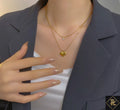 Mannequin wearing a dark blazer and white top with gold necklaces, one featuring a heart pendant.