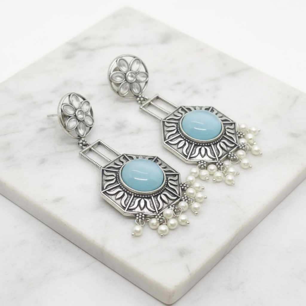 A pair of silver-toned dangle earrings with oval light blue stone centers, floral stud tops, and dangling pearl beads, displayed on a white marble slab.