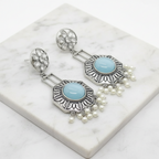 A pair of silver-toned dangle earrings with oval light blue stone centers, floral stud tops, and dangling pearl beads, displayed on a white marble slab.