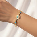 A gold-tone bracelet with three round turquoise blue stone accents, shown worn on a person's wrist against a soft white background.