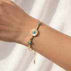A gold-tone bracelet with three round turquoise blue stone accents, shown worn on a person's wrist against a soft white background.