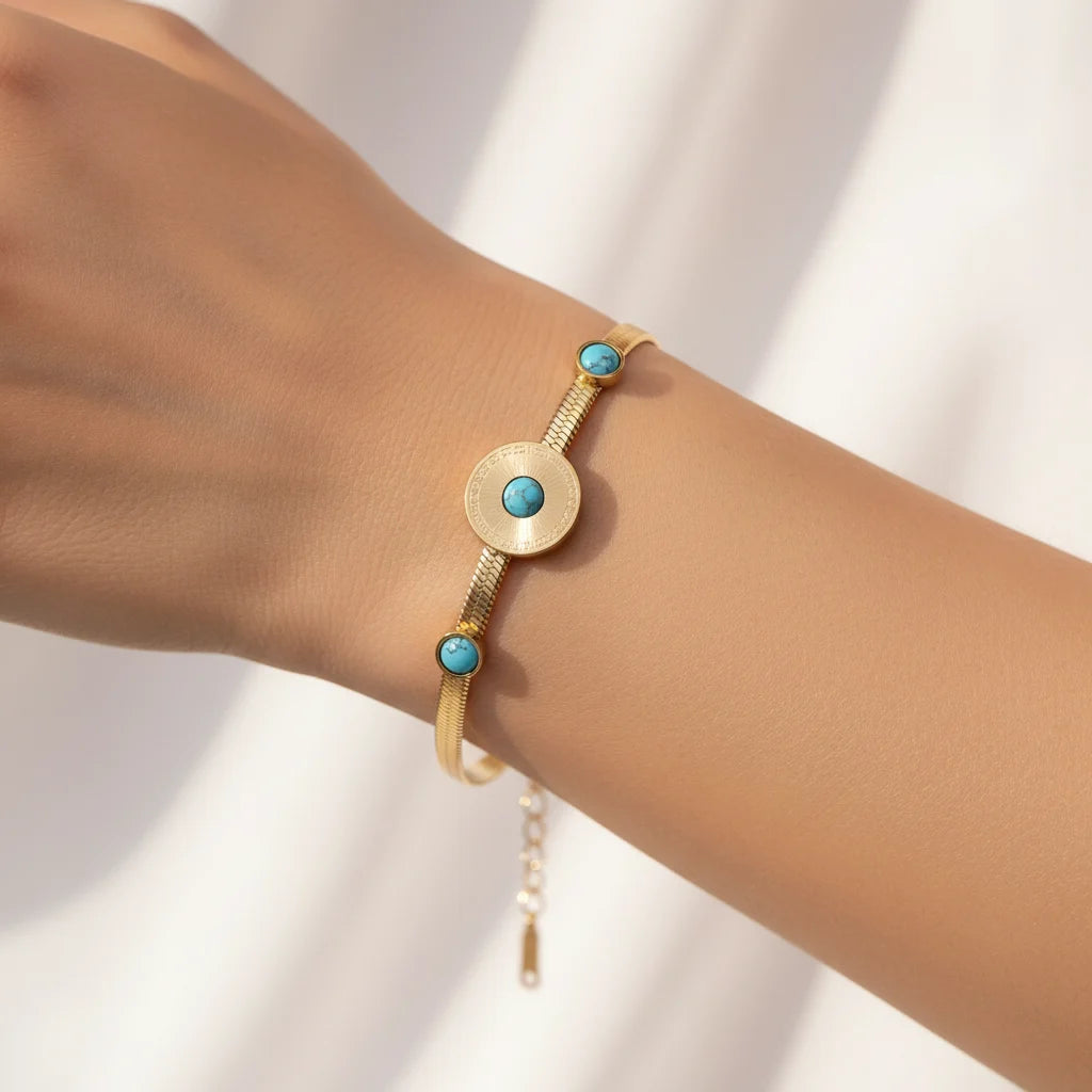 A gold-tone bracelet with three round turquoise blue stone accents, shown worn on a person's wrist against a soft white background.